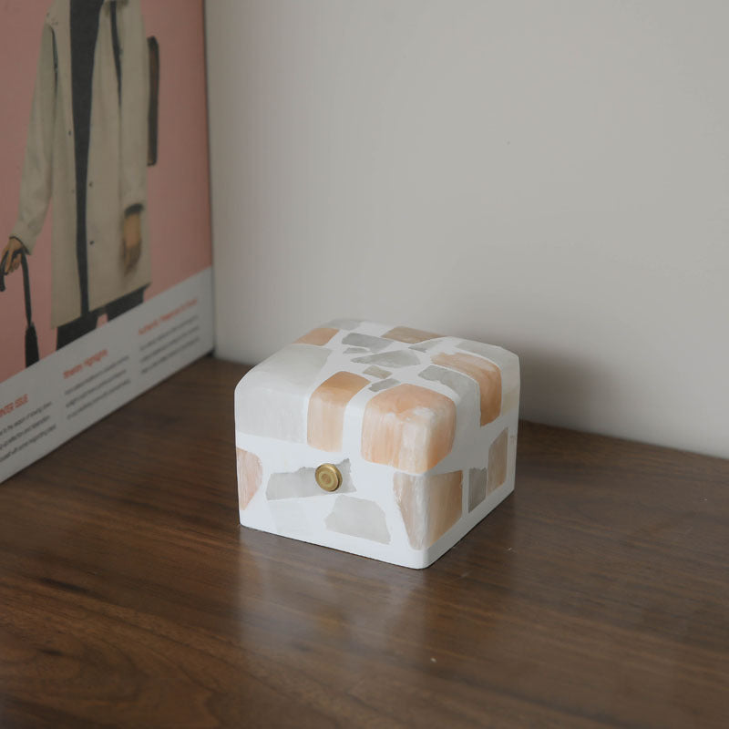 Unique crushed stone night light emitting a warm and calming glow through its textured surface. The night light is displayed on a bedside table, highlighting the beautiful natural stone patterns and providing a soothing ambiance to the room.