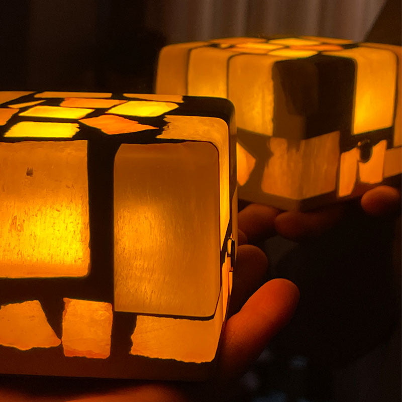 Unique crushed stone night light emitting a warm and calming glow through its textured surface. The night light is displayed on a bedside table, highlighting the beautiful natural stone patterns and providing a soothing ambiance to the room.