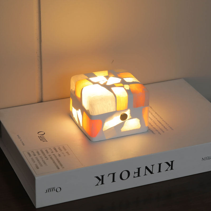 Unique crushed stone night light emitting a warm and calming glow through its textured surface. The night light is displayed on a bedside table, highlighting the beautiful natural stone patterns and providing a soothing ambiance to the room.