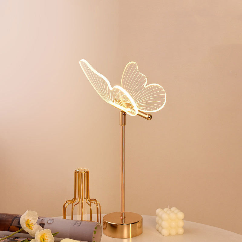 Charming Fairy Table Lamp featuring a delicate design with fairy silhouette cutouts, casting a warm and whimsical pattern of light and shadows when illuminated. The lamp is displayed on a wooden table, enhancing its magical and enchanting appeal.