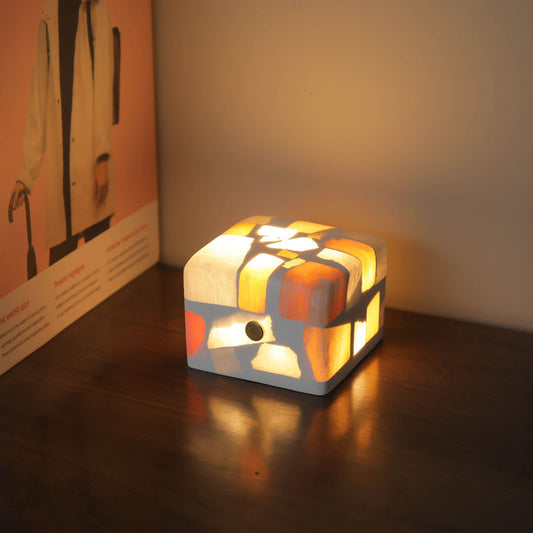 Unique crushed stone night light emitting a warm and calming glow through its textured surface. The night light is displayed on a bedside table, highlighting the beautiful natural stone patterns and providing a soothing ambiance to the room.